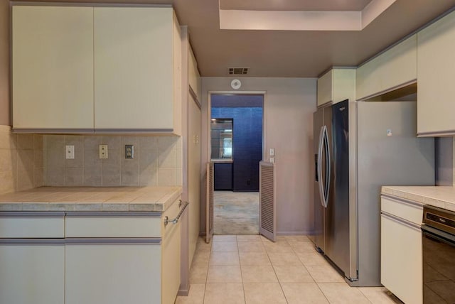 kitchen with light tile patterned floors, backsplash, a raised ceiling, and stainless steel refrigerator