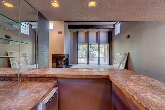 interior space with a wood stove, a textured ceiling, tile counters, and a healthy amount of sunlight