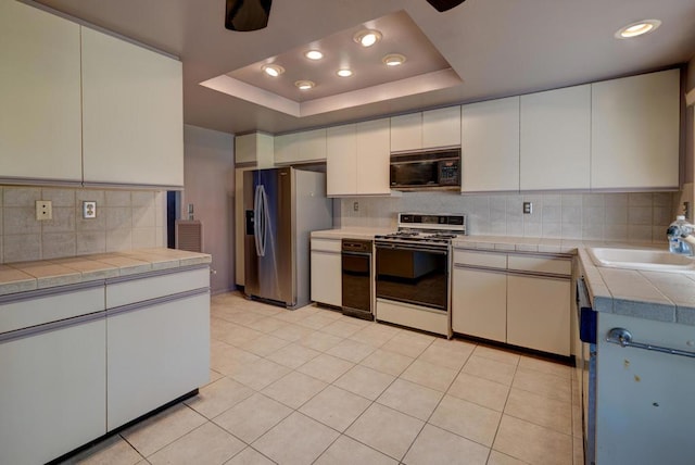 kitchen with white cabinets, range, sink, stainless steel fridge, and a raised ceiling