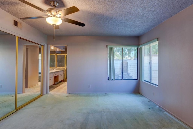 unfurnished bedroom featuring ceiling fan, ensuite bath, a closet, light colored carpet, and a textured ceiling