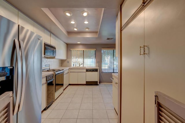 kitchen featuring stainless steel fridge, tasteful backsplash, a raised ceiling, white dishwasher, and gas range oven