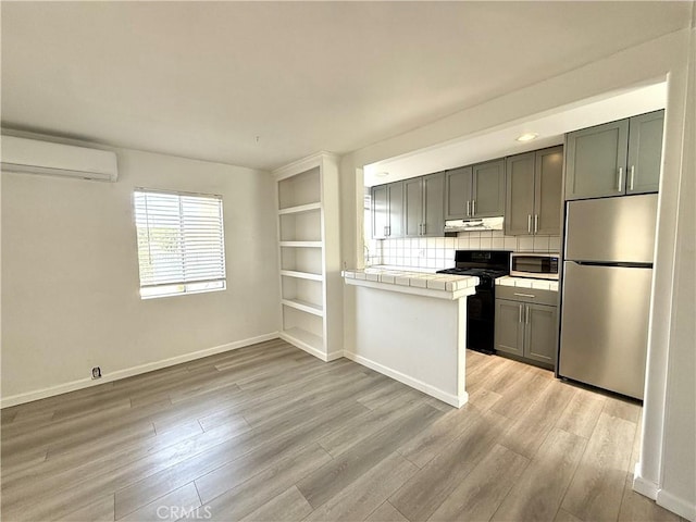 kitchen featuring a wall mounted air conditioner, tasteful backsplash, stainless steel appliances, tile countertops, and light hardwood / wood-style flooring