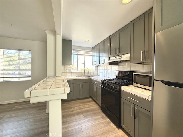 kitchen featuring tile countertops, black gas stove, white fridge, and a healthy amount of sunlight