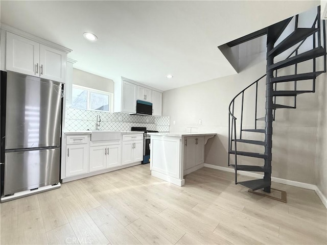 kitchen featuring white cabinetry, kitchen peninsula, a breakfast bar area, appliances with stainless steel finishes, and light wood-type flooring