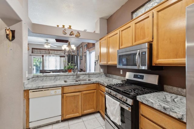 kitchen with appliances with stainless steel finishes, ceiling fan with notable chandelier, sink, light tile patterned floors, and light stone countertops