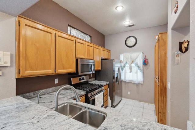 kitchen with appliances with stainless steel finishes, sink, light tile patterned floors, and light stone counters