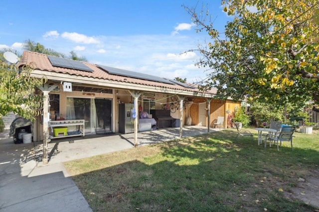 rear view of property with a lawn, a patio, and solar panels