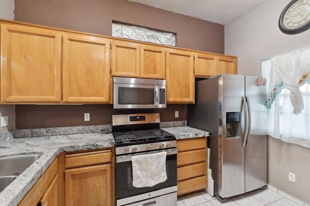 kitchen with light tile patterned flooring, appliances with stainless steel finishes, light stone countertops, and sink