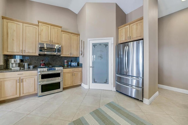 kitchen with light tile patterned flooring, appliances with stainless steel finishes, light brown cabinetry, and dark stone counters