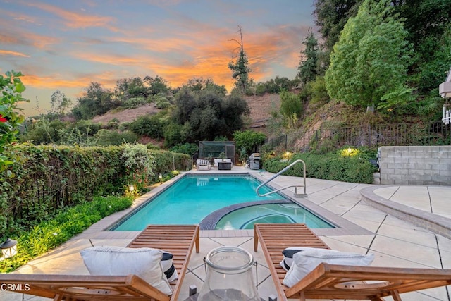 pool at dusk with an in ground hot tub and a patio