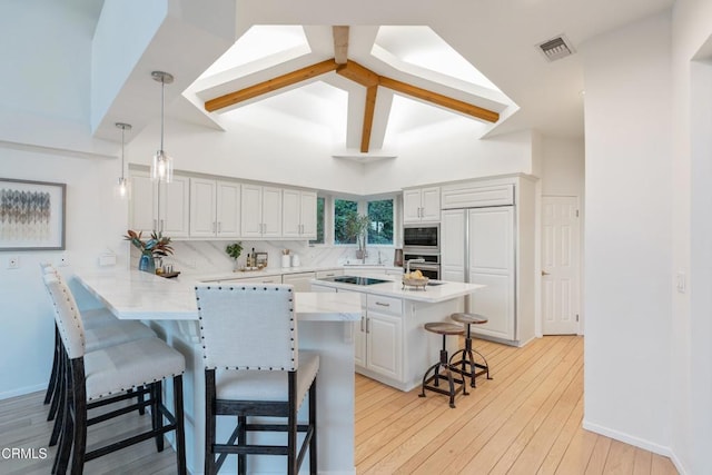 kitchen featuring kitchen peninsula, a kitchen breakfast bar, built in appliances, light hardwood / wood-style floors, and hanging light fixtures