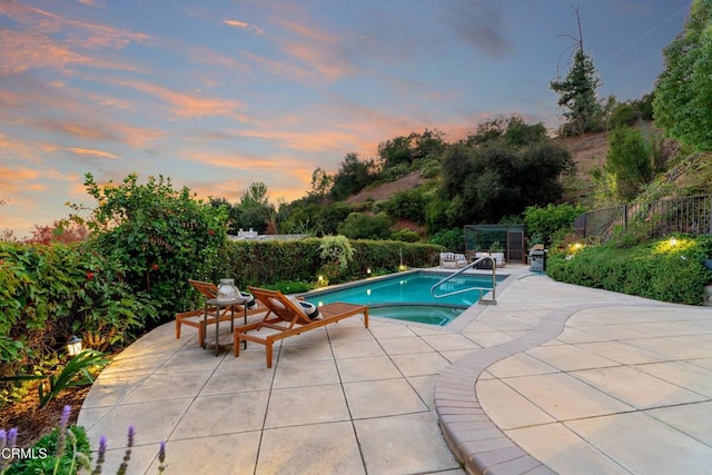 pool at dusk featuring a patio area and an in ground hot tub