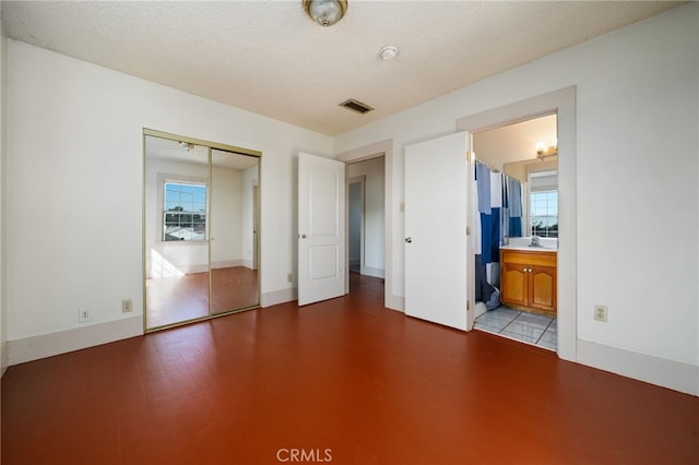 unfurnished bedroom with ensuite bath, a closet, multiple windows, and a textured ceiling