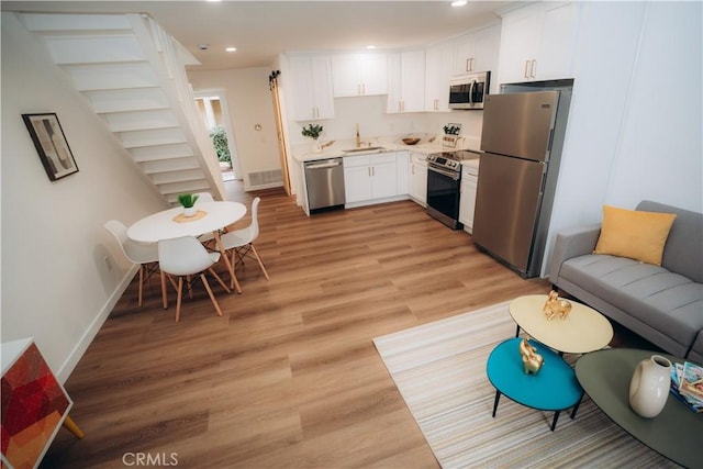 kitchen with sink, light hardwood / wood-style flooring, white cabinets, and appliances with stainless steel finishes