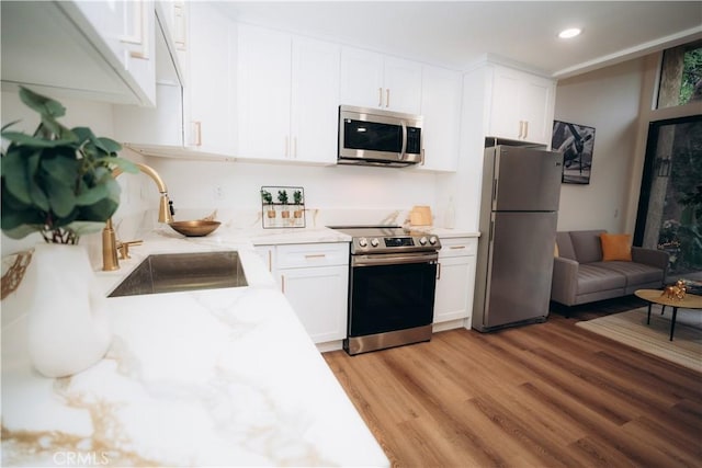 kitchen featuring appliances with stainless steel finishes, sink, white cabinets, light stone counters, and light hardwood / wood-style floors