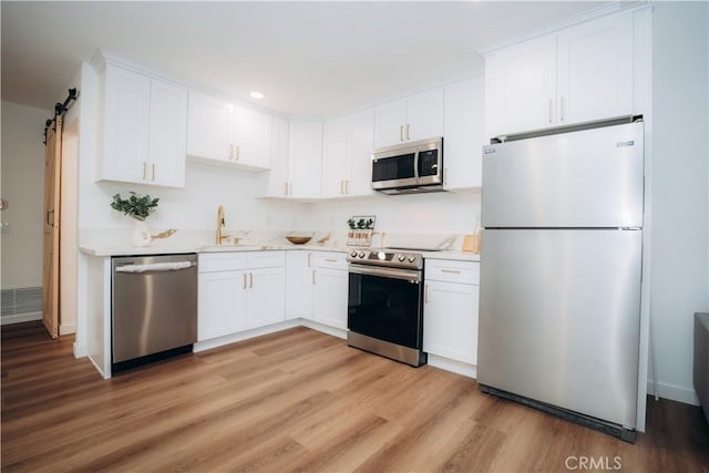 kitchen with white cabinetry, appliances with stainless steel finishes, a barn door, and sink