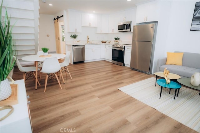 kitchen with sink, light wood-type flooring, stainless steel appliances, a barn door, and white cabinets