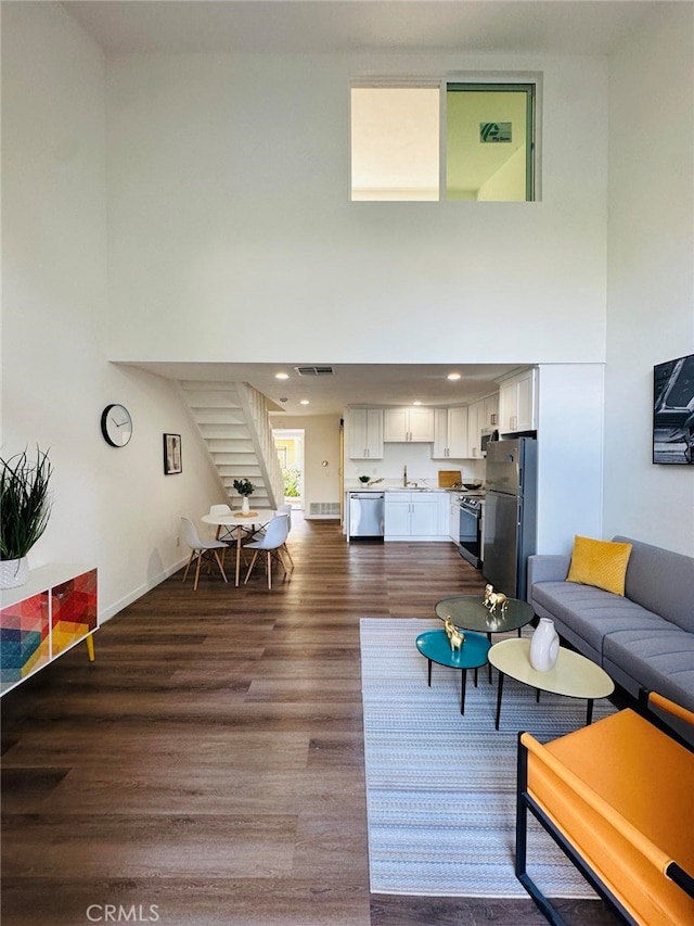 living room featuring sink, a towering ceiling, and dark wood-type flooring