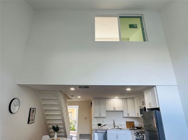 kitchen with white cabinetry, a towering ceiling, stainless steel appliances, and sink