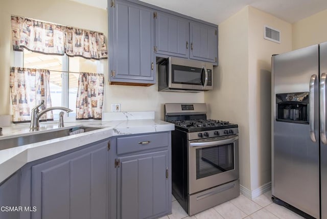 kitchen with light stone countertops, appliances with stainless steel finishes, sink, light tile patterned floors, and gray cabinets