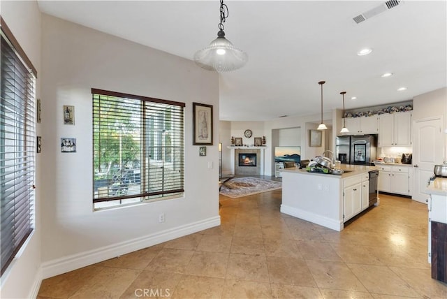 kitchen with white cabinets, decorative light fixtures, an island with sink, and stainless steel appliances