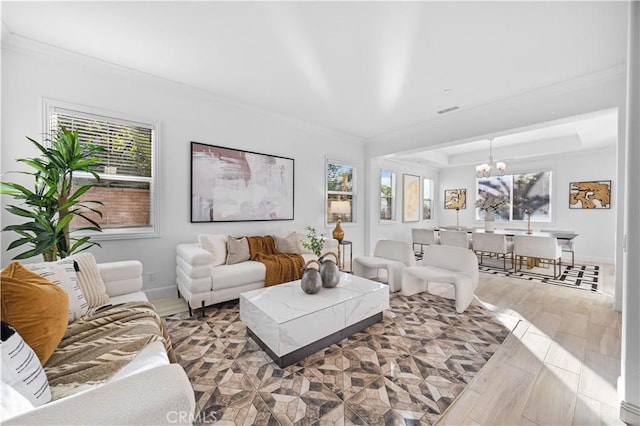 living room with a wealth of natural light, crown molding, light wood-type flooring, and a notable chandelier