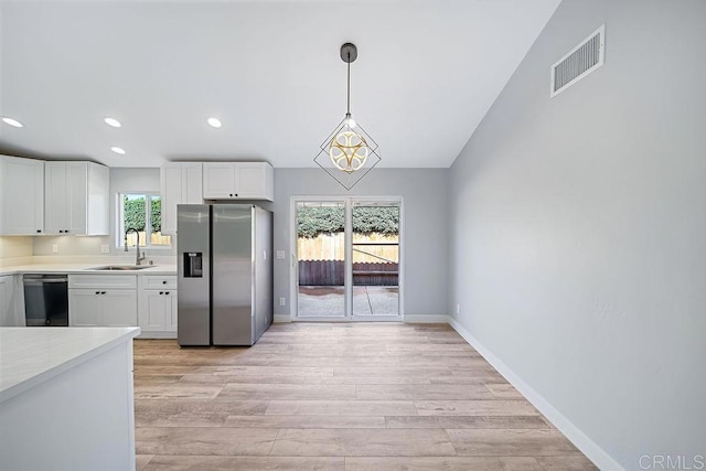 kitchen with a healthy amount of sunlight, white cabinetry, stainless steel appliances, and hanging light fixtures