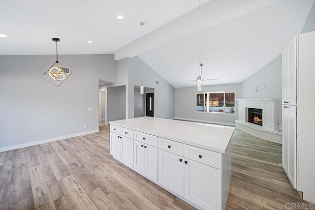 kitchen with lofted ceiling with beams, a brick fireplace, ceiling fan, light wood-type flooring, and white cabinetry