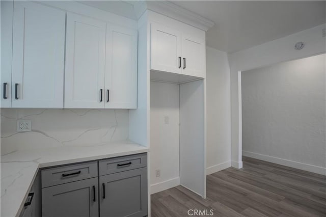 kitchen featuring decorative backsplash, light stone counters, white cabinetry, and light hardwood / wood-style flooring