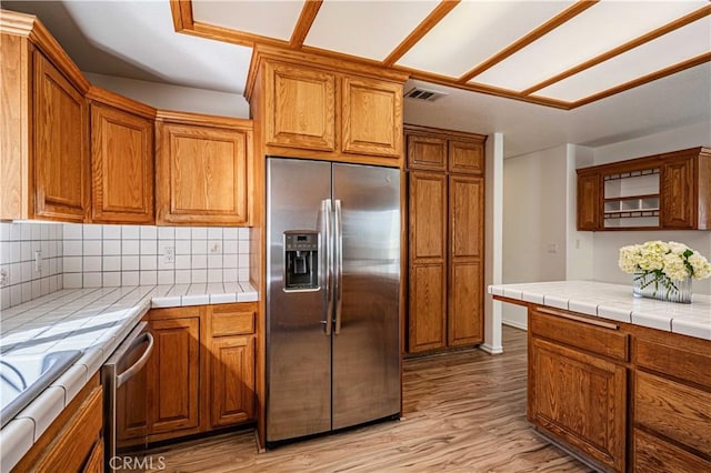 kitchen with decorative backsplash, tile counters, light hardwood / wood-style flooring, and appliances with stainless steel finishes