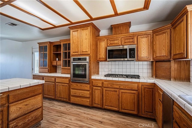 kitchen featuring tile countertops, decorative backsplash, light hardwood / wood-style flooring, and stainless steel appliances