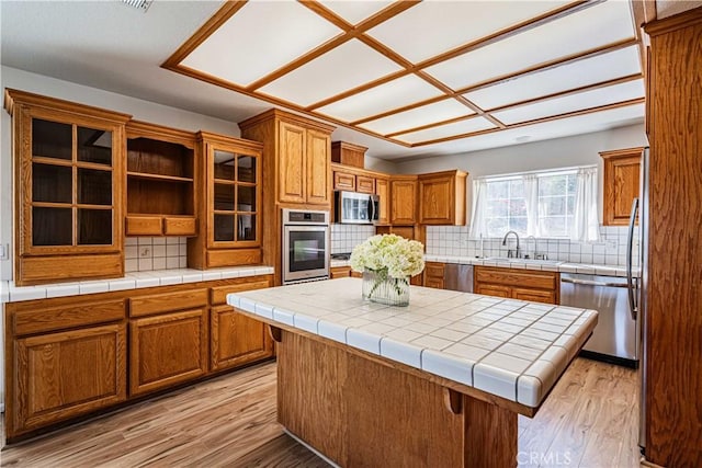 kitchen featuring tile countertops, a center island, light hardwood / wood-style flooring, tasteful backsplash, and stainless steel appliances