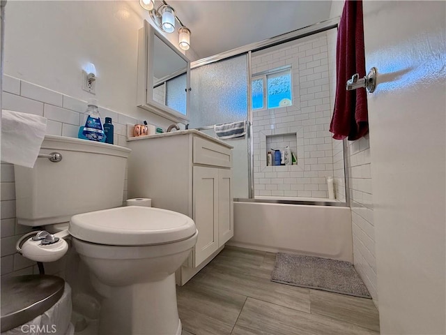 bathroom with combined bath / shower with glass door, toilet, and tile walls