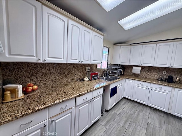 kitchen with white cabinetry, sink, dark stone counters, and lofted ceiling