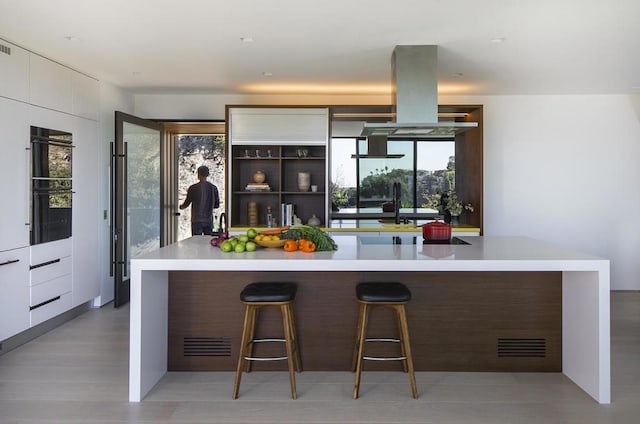 kitchen featuring white cabinetry, a center island, a kitchen breakfast bar, black double oven, and light wood-type flooring