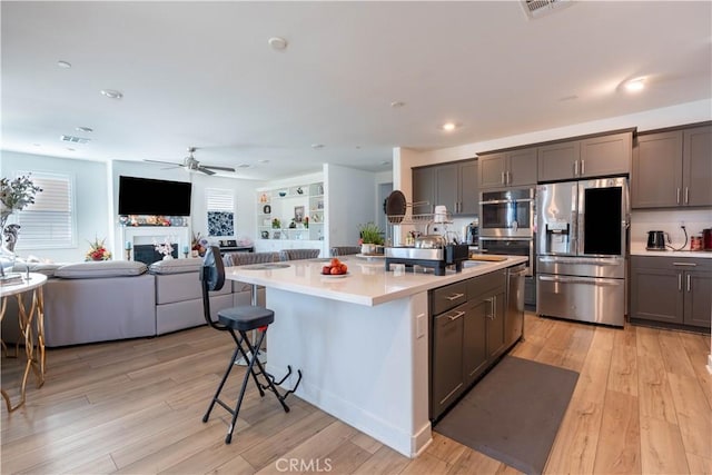 kitchen featuring a center island with sink, light hardwood / wood-style flooring, ceiling fan, a kitchen bar, and stainless steel appliances