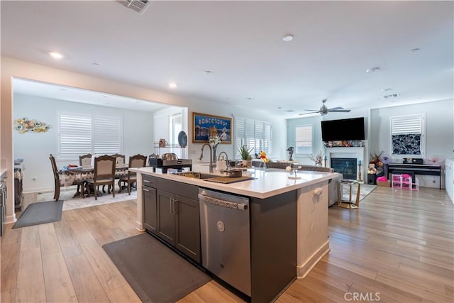 kitchen featuring ceiling fan, dishwasher, sink, a kitchen island with sink, and light wood-type flooring