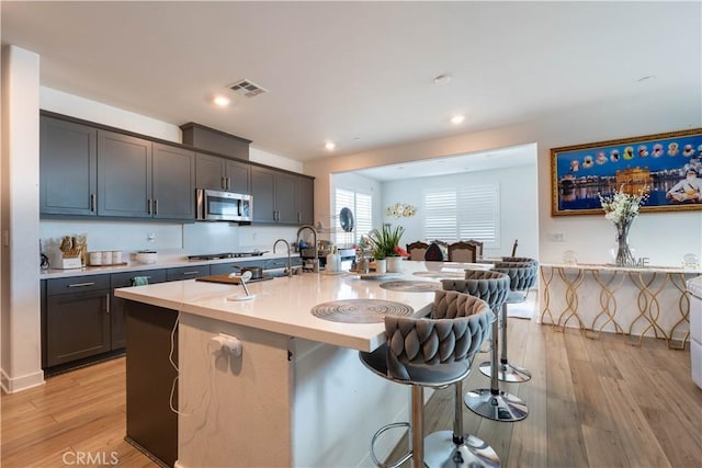 kitchen with a kitchen island with sink, sink, light wood-type flooring, a kitchen bar, and stainless steel appliances