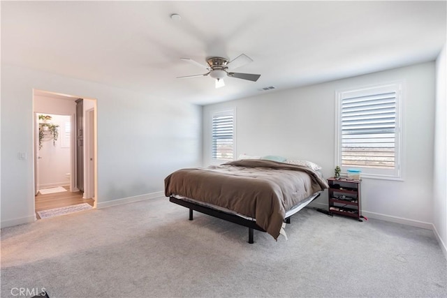 bedroom with ceiling fan, light colored carpet, and ensuite bath