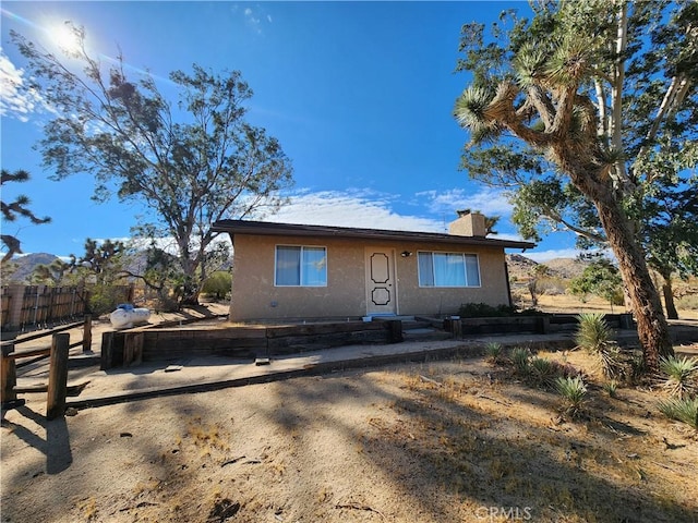 view of front of house featuring a chimney, fence, a mountain view, and stucco siding