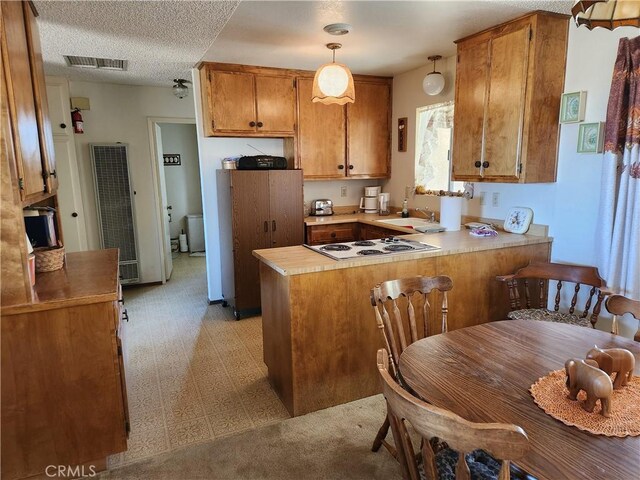 kitchen with white electric cooktop, kitchen peninsula, sink, hanging light fixtures, and a textured ceiling