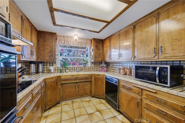 kitchen featuring tile countertops, black appliances, tasteful backsplash, and brown cabinetry