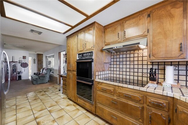 kitchen with tile counters, light tile patterned floors, decorative backsplash, and black appliances