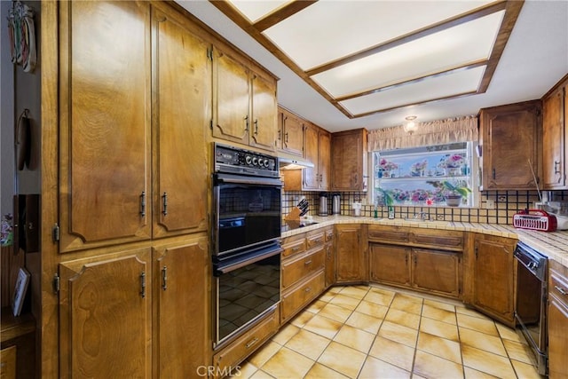 kitchen featuring tasteful backsplash, light tile patterned flooring, black appliances, brown cabinets, and under cabinet range hood