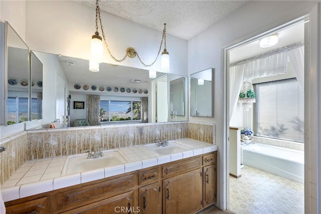 bathroom with double vanity, a textured ceiling, a sink, and tile patterned floors