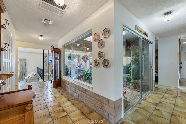 hall featuring light tile patterned floors, visible vents, and a textured ceiling