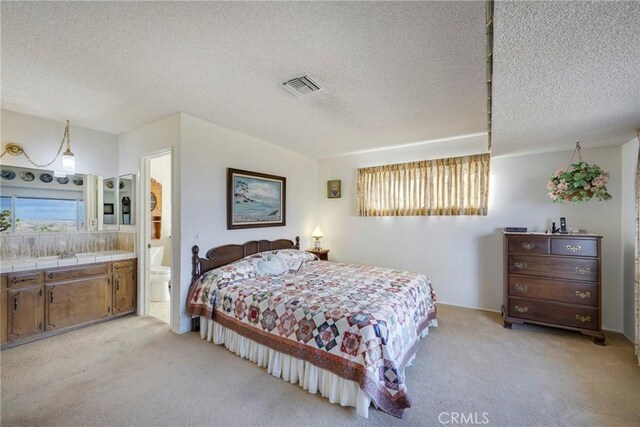 bedroom with a textured ceiling, light carpet, and ensuite bath