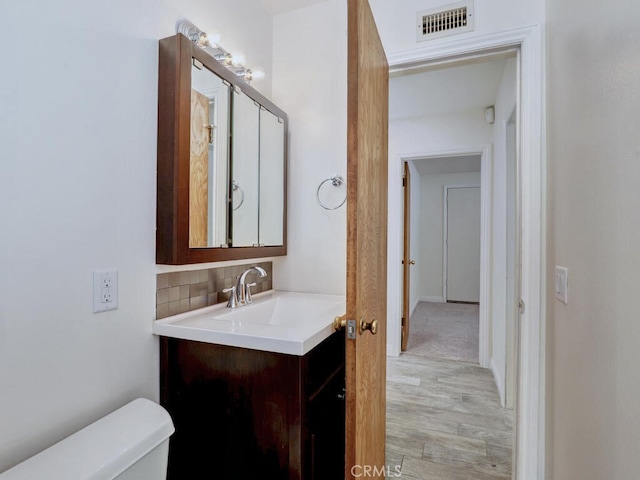 bathroom with vanity, toilet, wood-type flooring, and tasteful backsplash