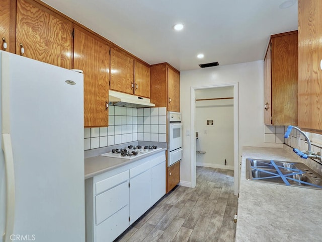 kitchen featuring light wood-type flooring, white appliances, tasteful backsplash, and sink