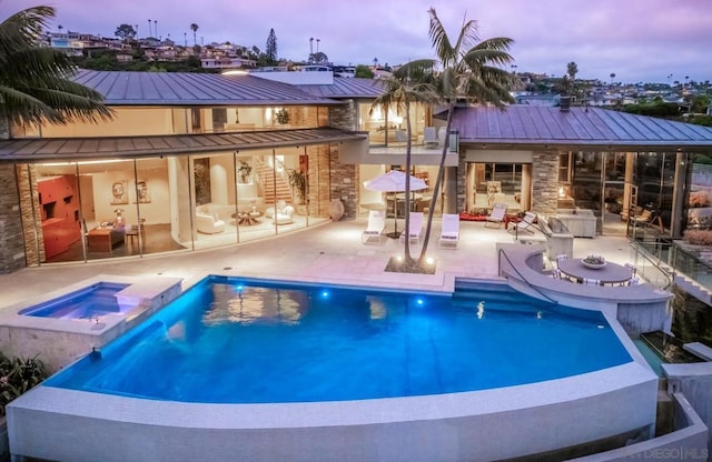 pool at dusk with an in ground hot tub and a patio